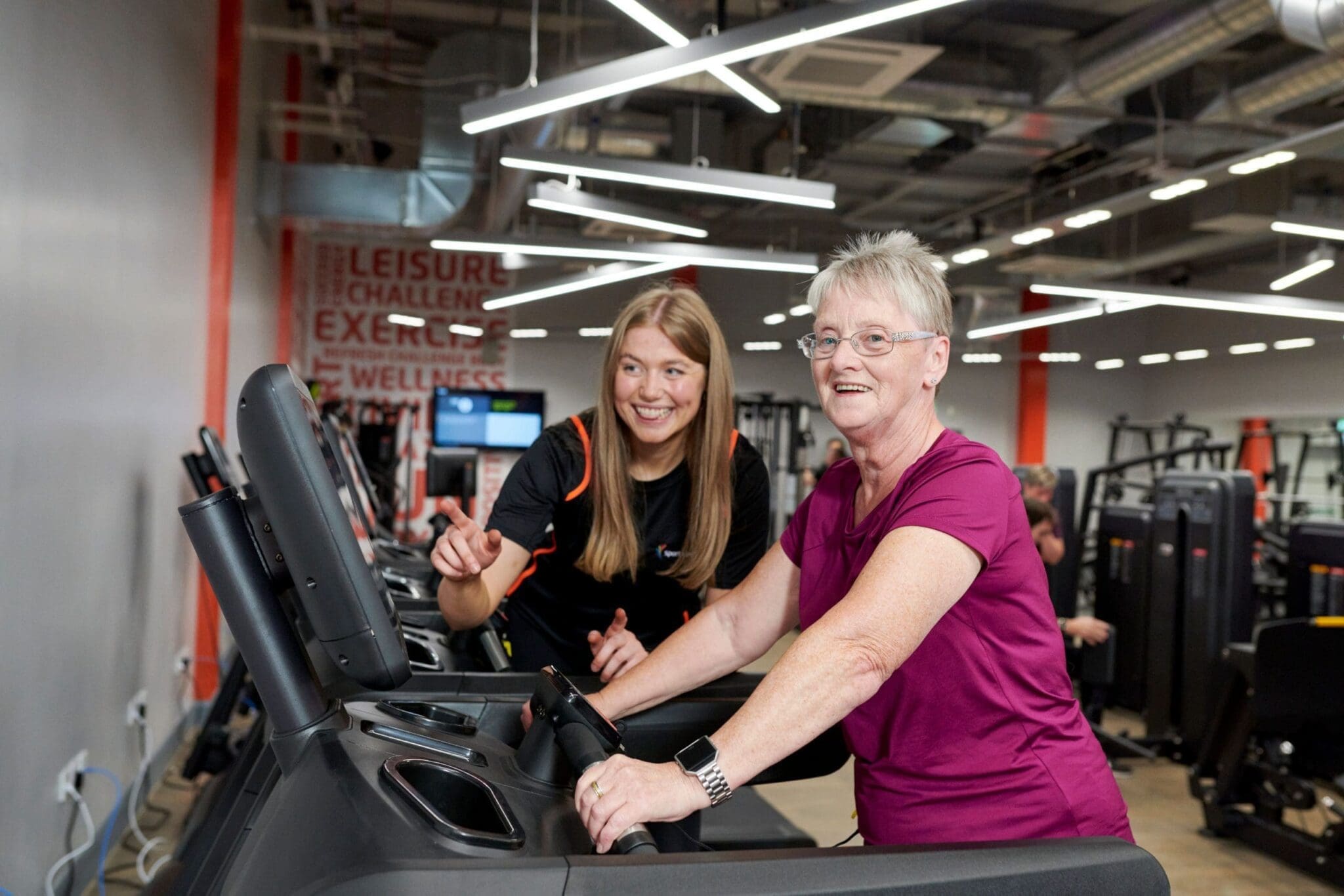 Advisor is helping an elderly woman with her workout at the gym.